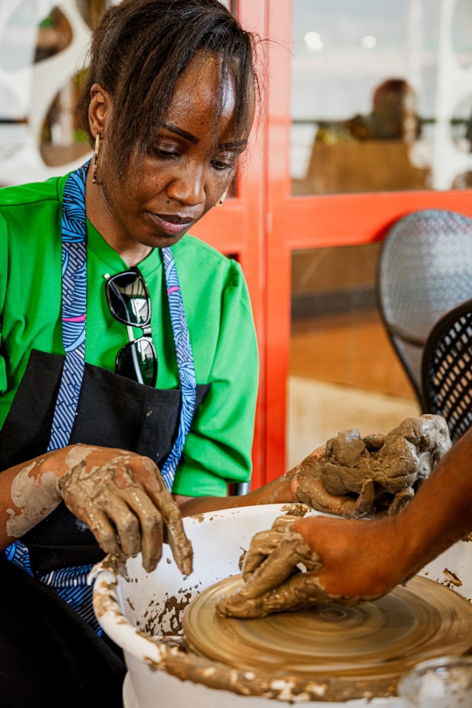 A participant in a bright green shirt works with an instructor at a pottery wheel