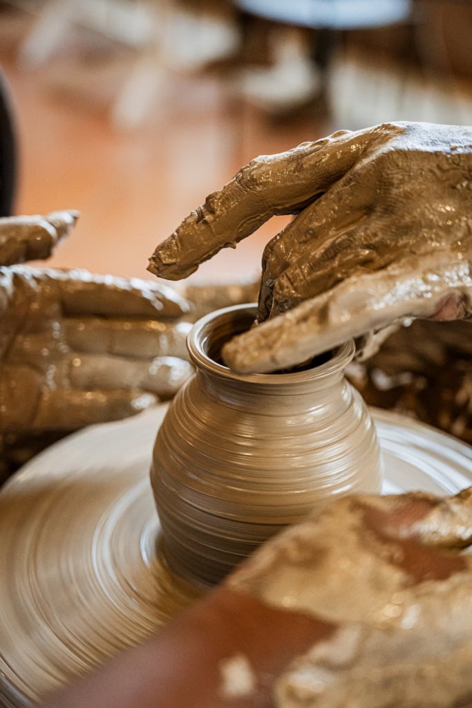 Clay-covered hands shaping a vessel on a spinning pottery wheel