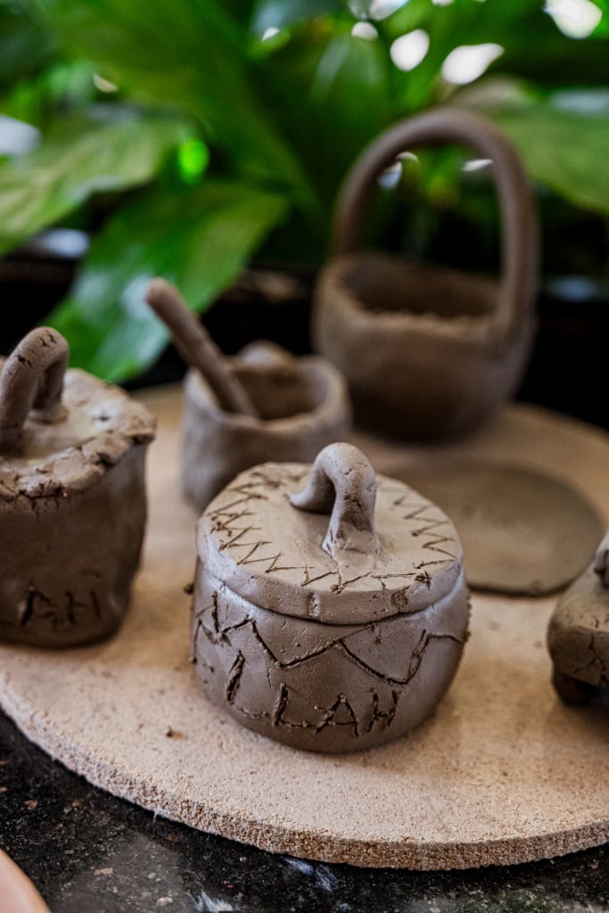 A small handmade clay pot with a looped handle sits among other clay vessels.