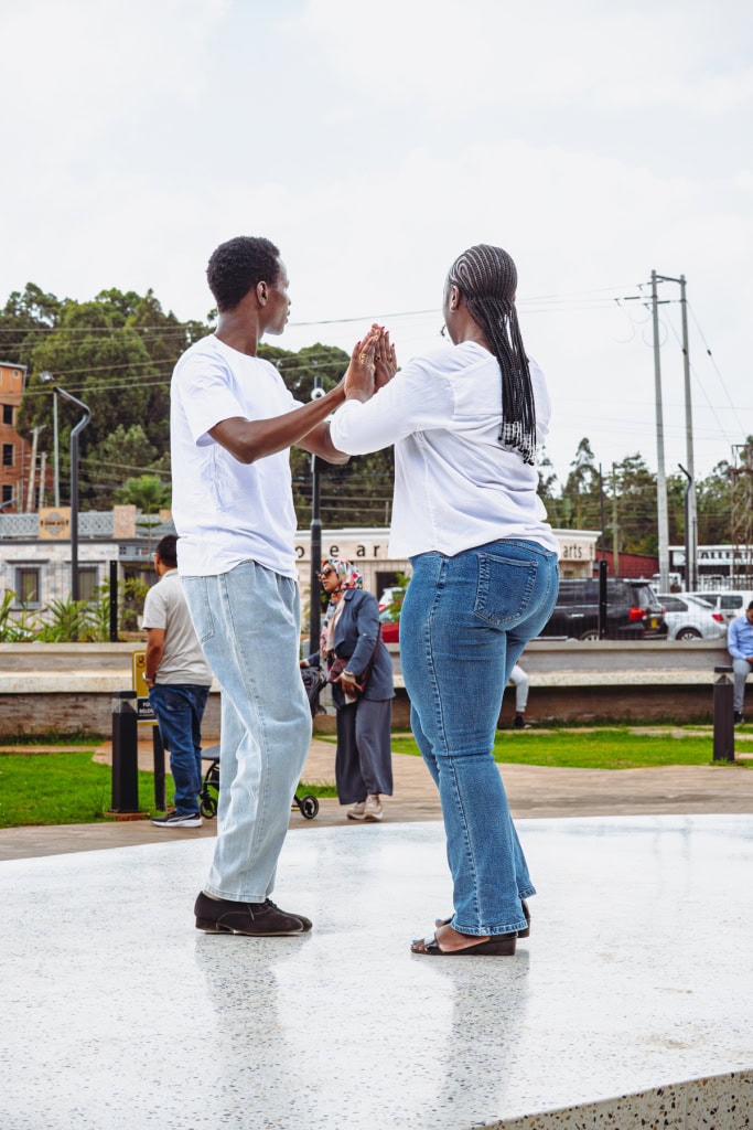 Two people in white shirts face each other with raised hands on an outdoor plaza