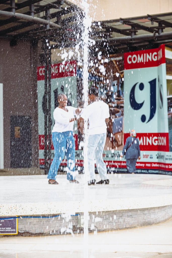 Two dancers perform on an outdoor stage as a fountain sprays in front of them.