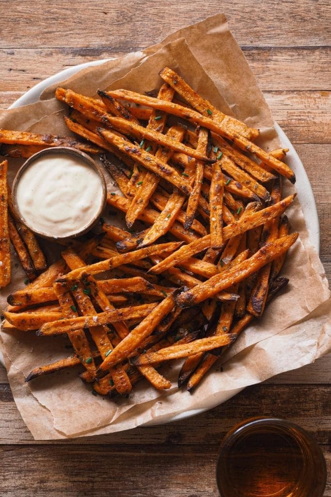 Boniatos Fritos al Horno, perfectos como aperitivo otoñal, guarnición o como pica pica si haceís plan para ver deporte con amigos por ejemplo. Son más saludables que si los hacemos fritos, súper fáciles y quedan realmente crujientes! Los acompaño con un dip de mayonesa especiada que puedes hacer picante o no al gusto. Aquí se ven los boniatos en un plato con el dip de mayonesa especiada en un bol pequeño y un vaso de cerveza en la parte inferior.