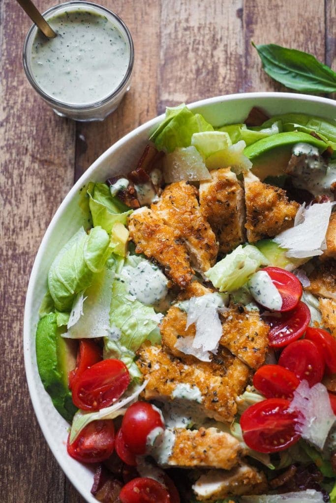 Ensalada de Pollo Crujiente y Panceta con Aliño de Tahini y Albahaca, una ensalada increíble y deliciosa, también perfecta como plato único. Es una combinación buenísima que hará que comer ensalada sea algo que disfrutes de verdad. Foto de cerca de la ensalada para que se aprecien bien los ingredientes: aguacate, tomates cherry, pollo crujiente, panceta, aliño, lechuga.