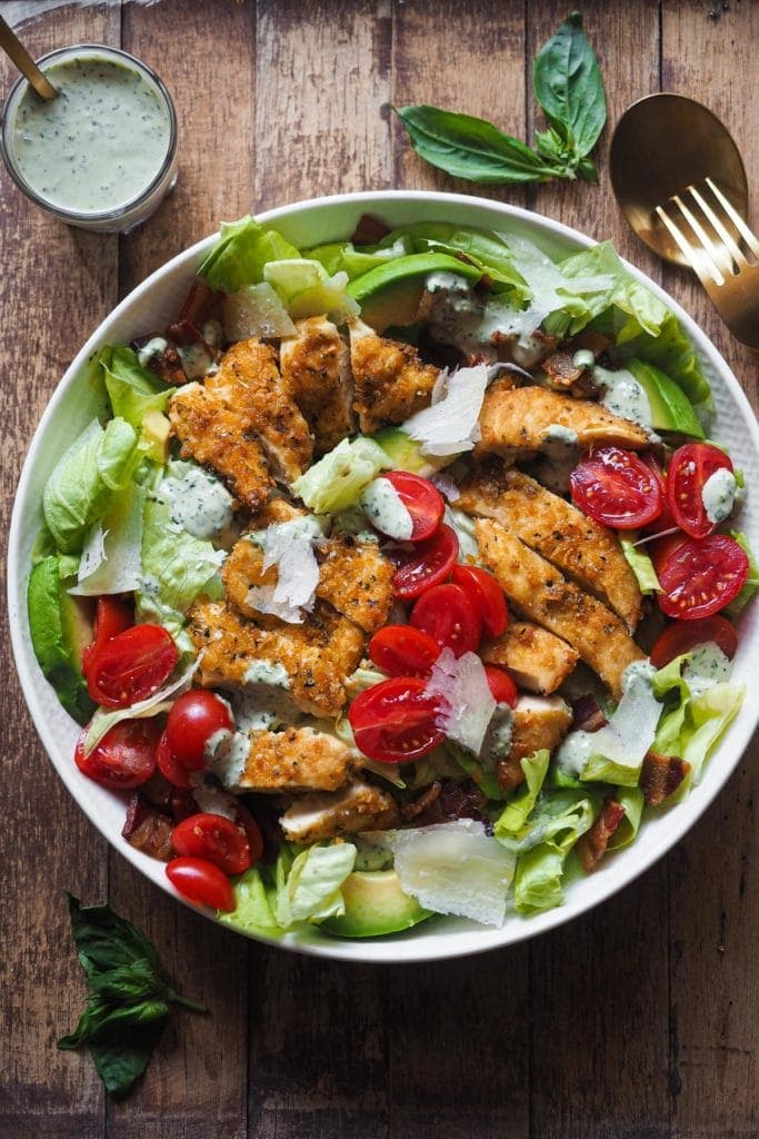 Crispy Chicken and Bacon Salad with Basil Tahini Dressing, an incredible salad that also makes a delicious meal. This salad combo is hard to beat and will make "Salad Meals" something to look forward to. The salad is placed in the middle of the shot, with a golden fork and a spoon on the top right corner and a little glass with extra dressing and a spoon in it on the top left corner.