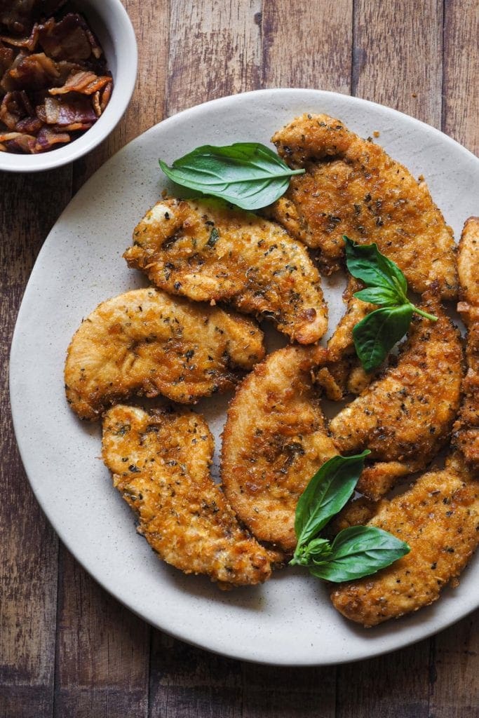 Ensalada de Pollo Crujiente y Panceta con Aliño de Tahini y Albahaca, una ensalada increíble y deliciosa, también perfecta como plato único. Es una combinación buenísima que hará que comer ensalada sea algo que disfrutes de verdad. Foto del pollo rebozado, ya cocinado. En la esquina superior izquierda hay un bol con panceta cocinada.