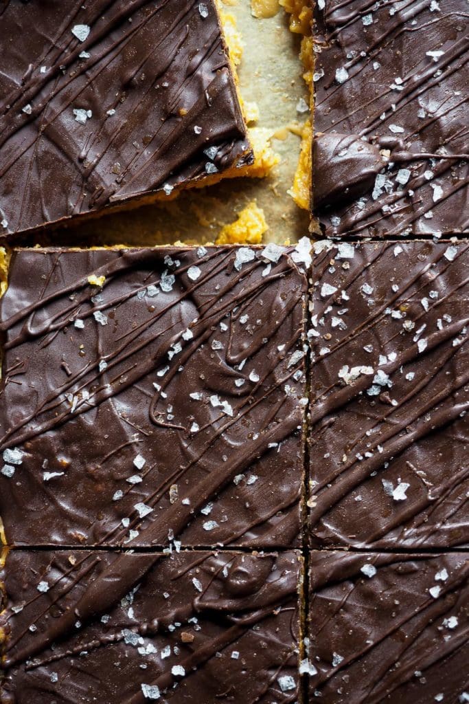 Healthy-ish Cornflakes and Nut Butter Bars, naturally gluten-free and vegan. They are easy and simple to make, and with that chocolate top, they are just the perfect snack. In this overhead shot, the bars are cut in squares and there's one a that seems to be pulled away from the rest on the top left corner. It's a close shot so the chocolate drizzle over the chocolate layer and the flaky sea salt can clearly be seen.