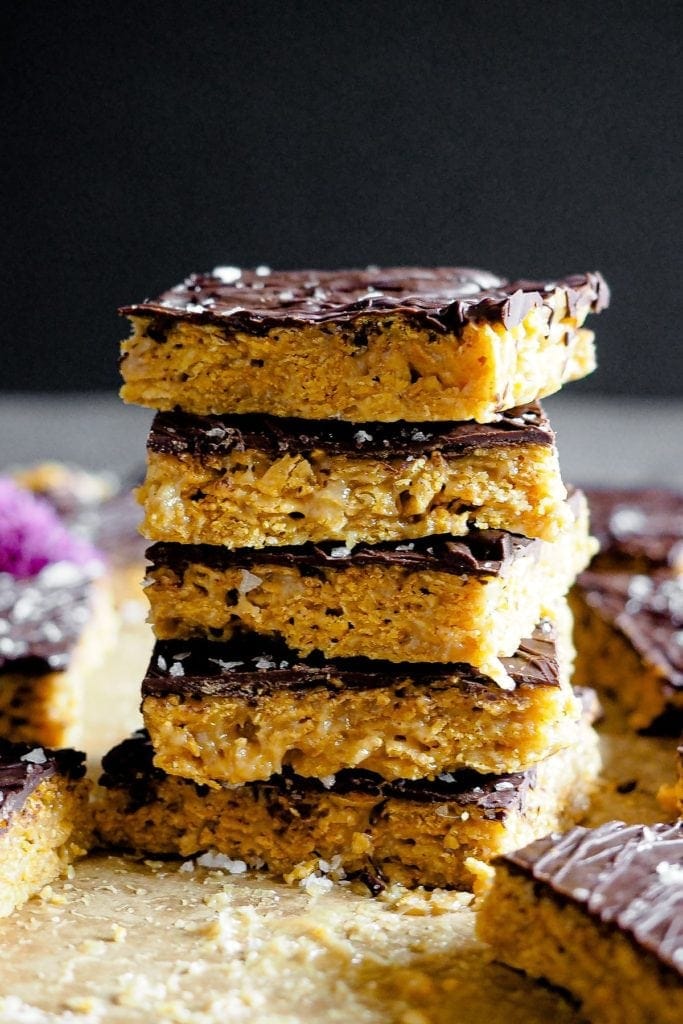 Healthy-ish Cornflakes and Nut Butter Bars, naturally gluten-free and vegan. They are easy and simple to make, and with that chocolate top, they are just the perfect snack. This is a 90 degree angle shot of the bars layering one on top of each other. The gooey crunchy cornflakes, chocolate and flaky sea salt can be clearly distinguished.