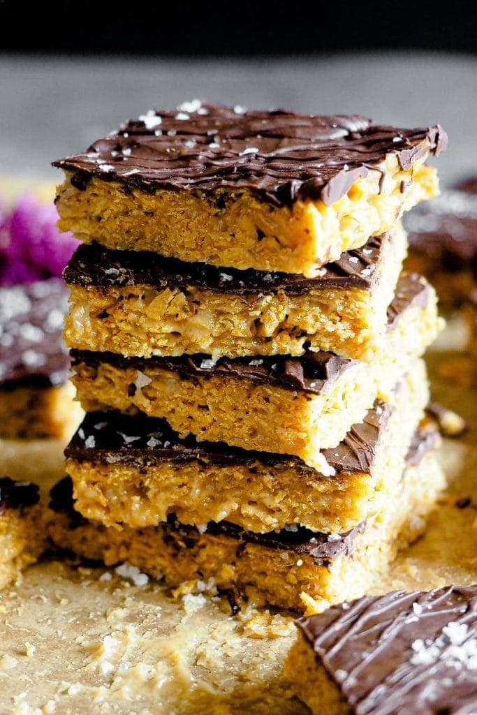 Healthy-ish Cornflakes and Nut Butter Bars, naturally gluten-free and vegan. They are easy and simple to make, and with that chocolate top, they are just the perfect snack. This is a 30 degree angle shot of the bars layering one on top of each other. The gooey crunchy cornflakes, chocolate and flaky sea salt can be clearly distinguished.