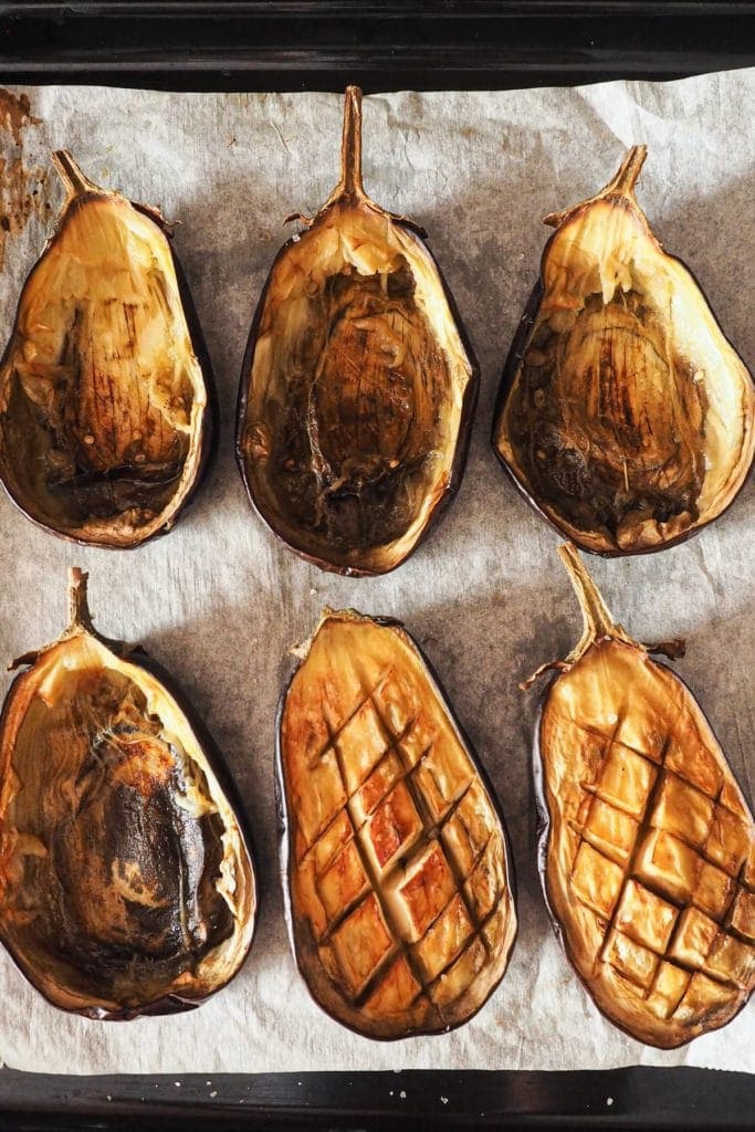 Sausage Stuffed Aubergine out of the oven. Some skins are already empty and there are 2 halves with scored flesh waiting to be removed.