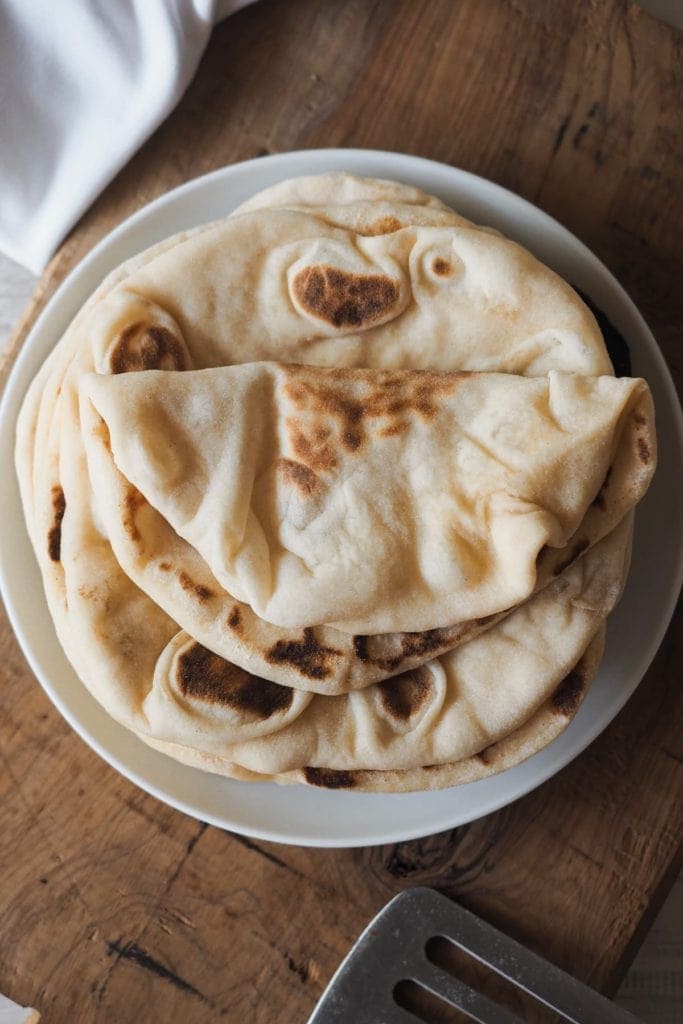 This delicious, pillowy soft Turkish Flatbread is simply incredible! It’s extra soft, tender and hollow, a perfect cross between Naan bread and Pita bread. Serve alongside your favourite saucy dishes, with grilled meats, hummus, or simply on its own. Overhead shot of a plate with a few bazlamas. The one at the very top is folded.