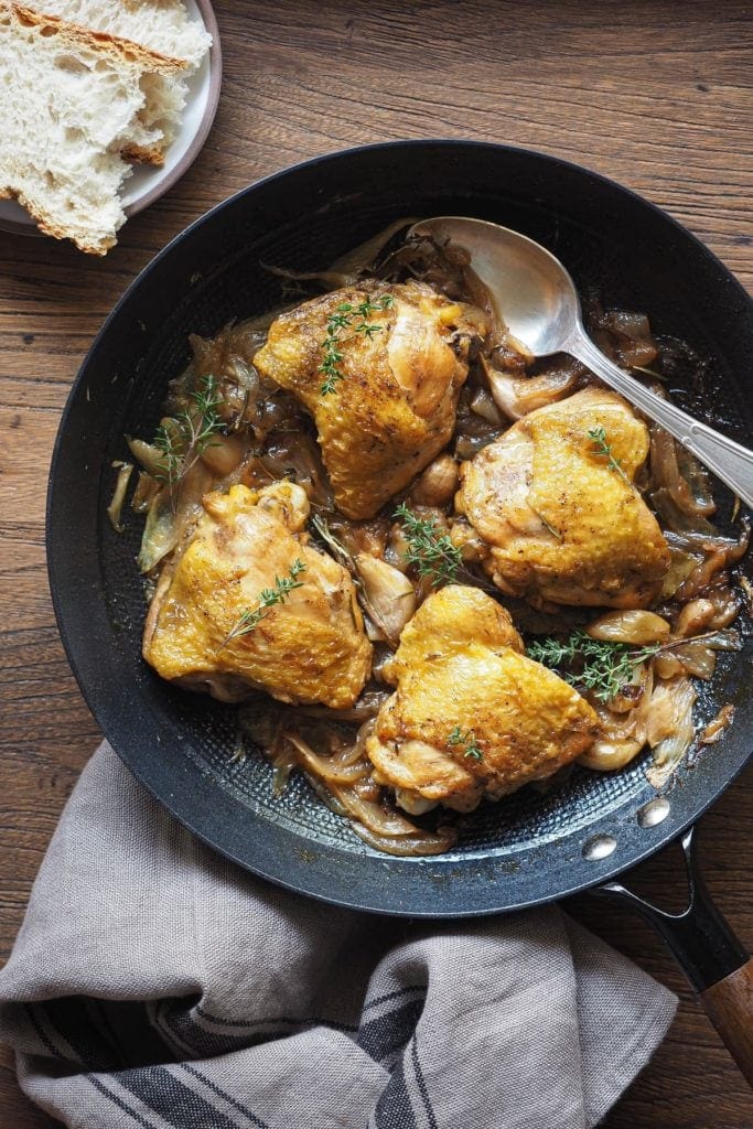 Jugoso Pollo al Cava (o Pollo al Champagne), sencillo, lleno de sabor y te hace quedar genial si tienes una comida con amigos o familia! Lleva cebolla y ajo, que quedan a punto de caramelo, y hierbas aromáticas para añadir un toque más de sabor. Es perfecto para hacer en modo batchcooking y así tener para más de un día. Y bueno, qué decir de las recetas de la abuela... ¡nunca fallan! Aquí el pollo se ve servido en una sartén profunda de hierro, con pan a un lado y un trapo en otro. El pollo está decorado con tomillo fresco.