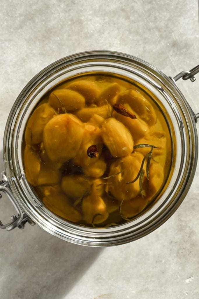 Esta receta de Ajos Confitados (o Confit de Ajo) se va a convertir en tu nuevo indispensable en la cocina porque es tan fácil y los ajos confitados son taaaaaan espectaculares y versátiles. Solo necesitas unas cuantas cabezas de ajo, tus especias y hierbas favoritas, mucho aceite de oliva y 30 minutos. El resultado es un ajo que se deshace como mantequilla, con un sabor dulzón y que puedes usar de mil maneras. Además, como bonus te queda un aceite de ajo insuperable. | Receta de Paula's Apron