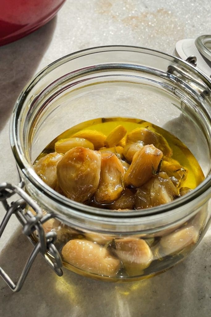 This Garlic Confit recipe is going to become your new pantry staple because it's so easy and confited garlic is so spectacular and versatile. You just need a few heads of garlic, your favourite spices and herbs, lots of olive oil and 30 minutes. The result is a scrumptious sort of sweet spreadable garlic that you can use in a thousand ways. As a bonus, you get garlic-infused oil! | Paula's Apron Recipe