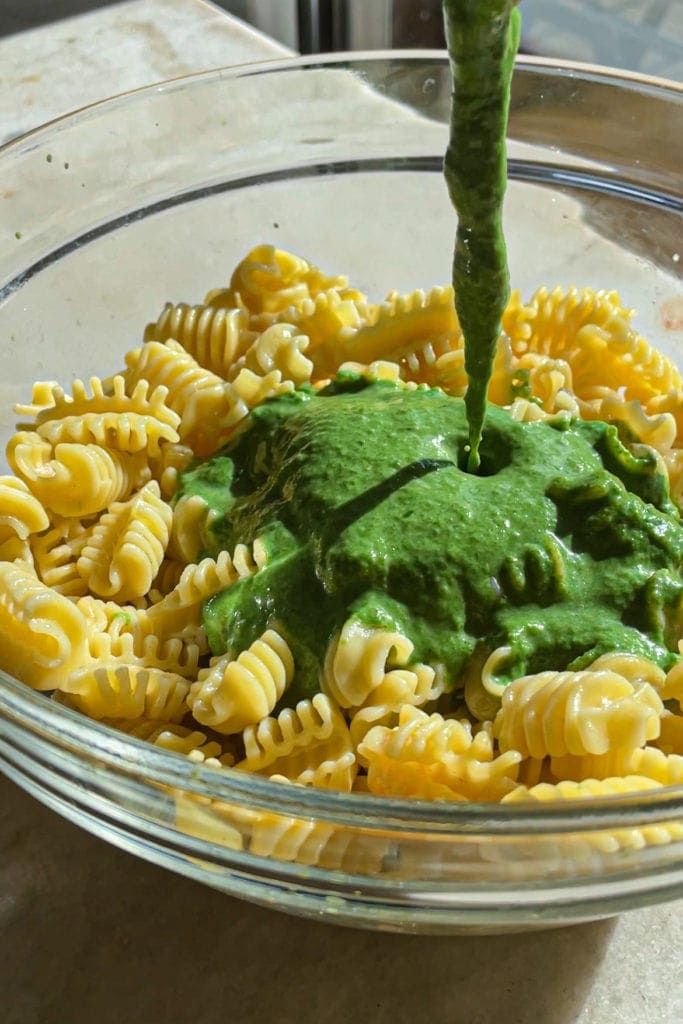 Short pasta with a delicious spinach and ricotta sauce. The sauce is being poured over the pasta in a bowl. | Paula's Apron Recipe