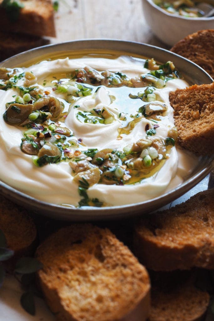 This Garlic Confit Goat Cheese Dip with Spicy Lemony Olives is creamy, tasty and easy to make. Oh! And it's a 3 in one dip: a spreadable garlic confit cheese base, homemade toasts and the most delicious olive topping. It makes a delicious appetiser and it's perfect for any occasion and all year round! | Paula's Apron Recipe