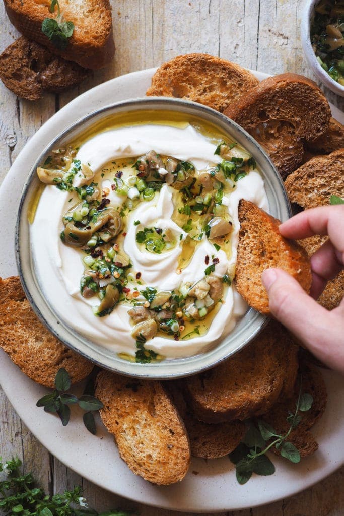 This Garlic Confit Goat Cheese Dip with Spicy Lemony Olives is creamy, tasty and easy to make. Oh! And it's a 3 in one dip: a spreadable garlic confit cheese base, homemade toasts and the most delicious olive topping. It makes a delicious appetiser and it's perfect for any occasion and all year round! | Paula's Apron Recipe