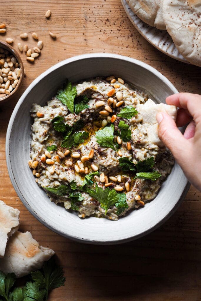 El Mutabal es un dip de berenjena muy parecido al Baba Ganoush con la gran diferencia de que el primero lleva tahini y no lleva melaza de granada. Es un aperitivo ideal o snack saludable, incluso va genial como acompañamiento. Es un dip cremoso, con un sabor meloso gracias a ese toque ahumado de la berenjena asada. Además es vegano (o se puede adaptar fácilmente), sin gluten y lo mejor, muy fácil de hacer. Acompáñalo de verduras o algún tipo de pan plano y listos, ya solo queda disfrutarlo. | Receta de Paula's Apron