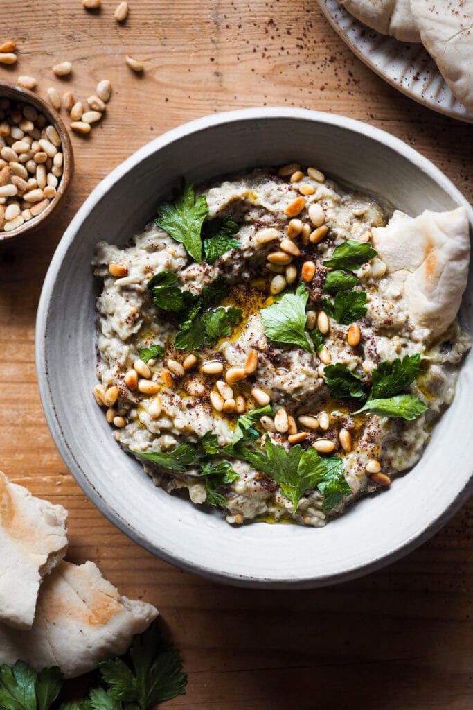 El Mutabal es un dip de berenjena muy parecido al Baba Ganoush con la gran diferencia de que el primero lleva tahini y no lleva melaza de granada. Es un aperitivo ideal o snack saludable, incluso va genial como acompañamiento. Es un dip cremoso, con un sabor meloso gracias a ese toque ahumado de la berenjena asada. Además es vegano (o se puede adaptar fácilmente), sin gluten y lo mejor, muy fácil de hacer. Acompáñalo de verduras o algún tipo de pan plano y listos, ya solo queda disfrutarlo. | Receta de Paula's Apron