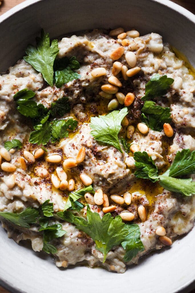 El Mutabal es un dip de berenjena muy parecido al Baba Ganoush con la gran diferencia de que el primero lleva tahini y no lleva melaza de granada. Es un aperitivo ideal o snack saludable, incluso va genial como acompañamiento. Es un dip cremoso, con un sabor meloso gracias a ese toque ahumado de la berenjena asada. Además es vegano (o se puede adaptar fácilmente), sin gluten y lo mejor, muy fácil de hacer. Acompáñalo de verduras o algún tipo de pan plano y listos, ya solo queda disfrutarlo. | Receta de Paula's Apron