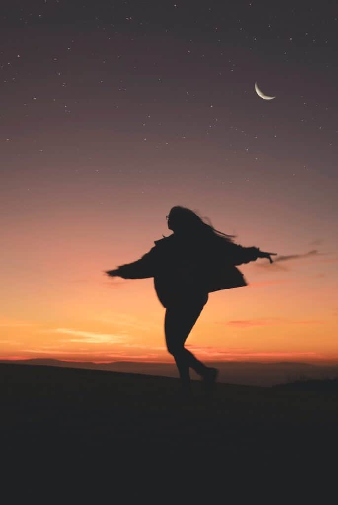 silhouette of woman dancing against sunset background with crescent moon