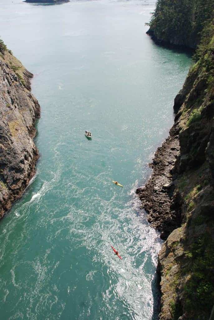 View of boat and kayak in busy water with cliffs on either side, from above, Deception Pass, Fidalgo and Whidbey Islands, San Juan Islands, Washington