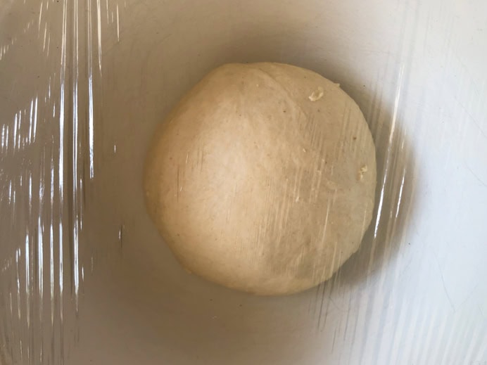 Pizza dough proving in a bowl covered with cling film.