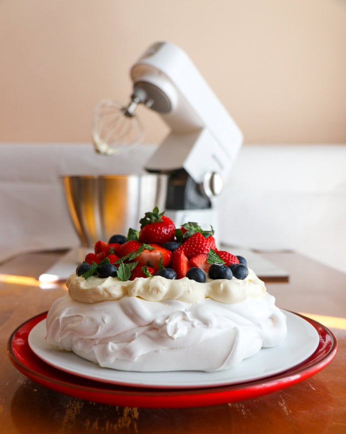 Pavlova recipe with whipped cream, strawberries and raspberry coulis in front of a Kenwood Chef stand mixer.