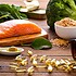 Front view of many fish oil capsules spilling out from the bottle surrounded by an assortment of food rich in omega-3 such as salmon, flax seeds, broccoli, sardines, spinach, olives and olive oil.