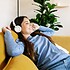 Relaxed smiling young adult woman with headphones sitting on sofa at home