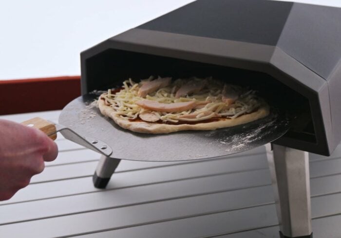 pizza being put into a vevor gas pizza oven with the included pizza peel