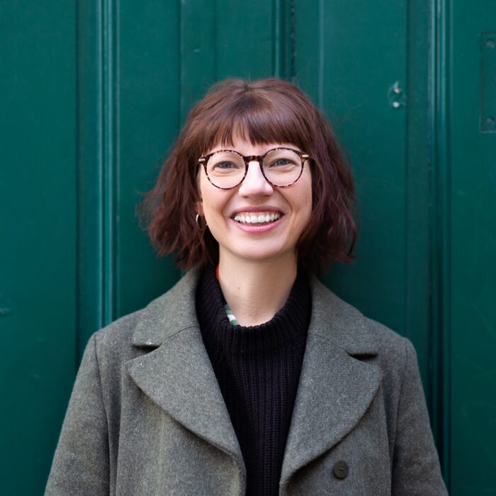 Die Illustratorin und Autorin Raffaela Schöbitz steht vor einer grünen Wand und lacht in die Kamera