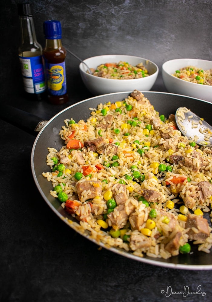 Leftover roast pork fried rice in frying pan, served bowls in the background.