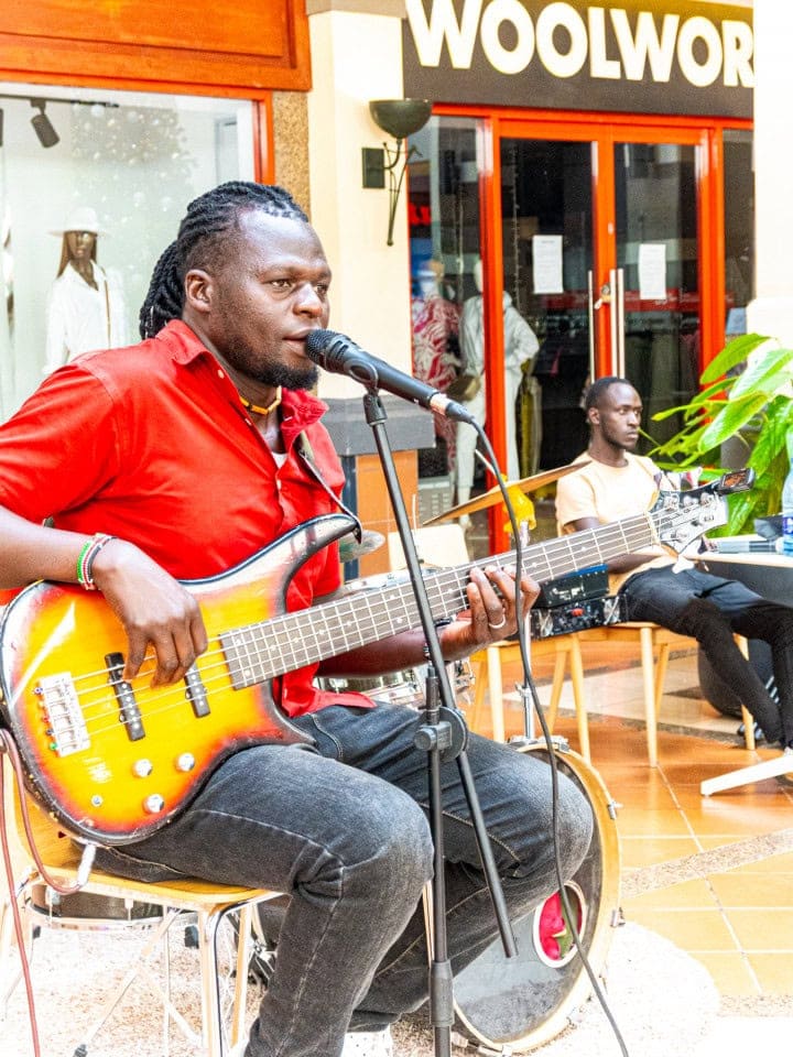 Musician in a red shirt singing into a microphone while playing bass guitar