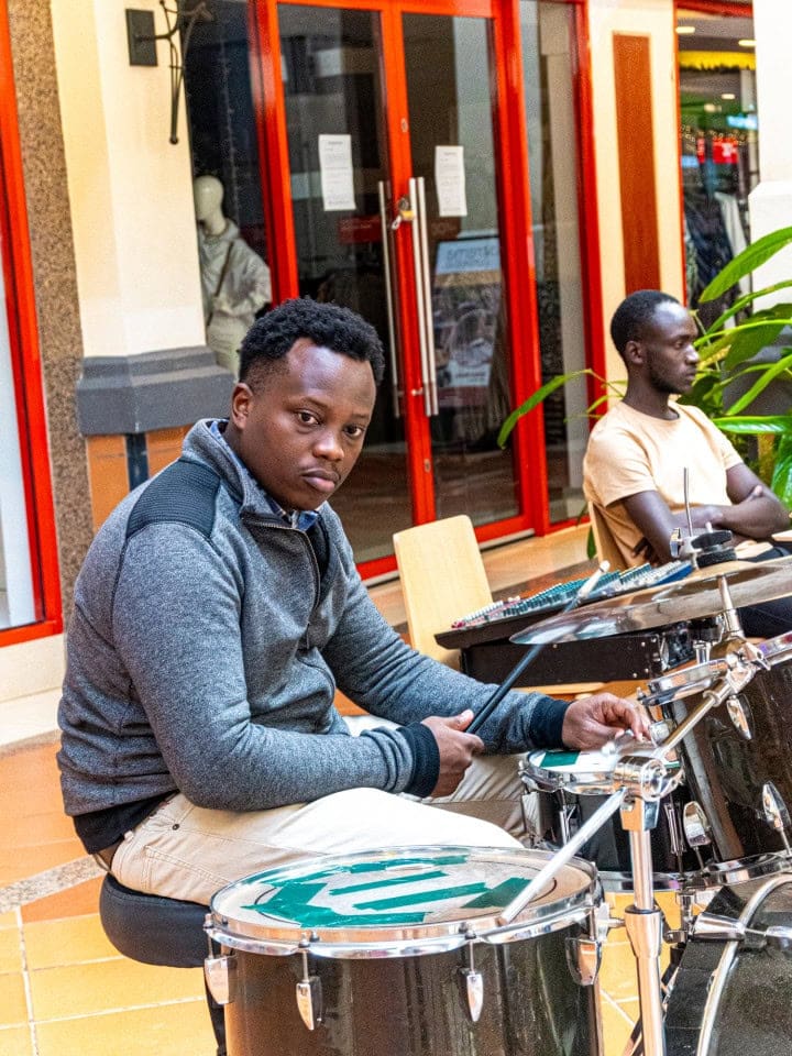 Musician playing a drum kit while another musician sits behind him