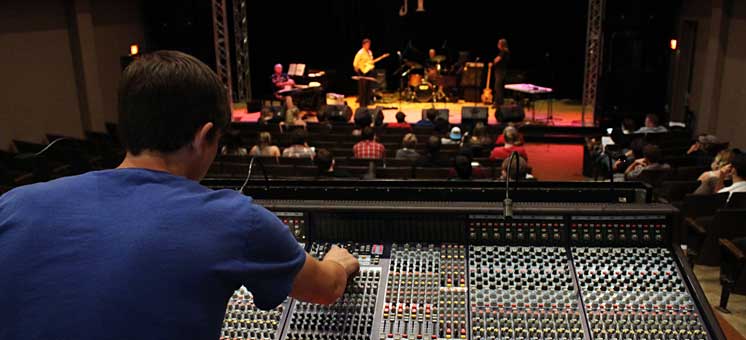 Photo of Front of House Mixing Engineer at soundboard front of house with view of stage