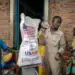 A Burundian government official speaks with newly arrived Congolese refugees awaiting relocation while weighing a sack of rice from the final batches delivered by the now-dismantled US Agency for International Development (USAID). [Luis Tato/AFP]