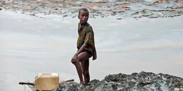 A boy with a fishing net stands on the oil-soaked bank of a creek area in the Niger Delta: children are particularly susceptible to environmental pollutants, absorbing it into their tissue more rapidly than adults. Image by Milieudefensie via Flickr (CC BY-NC-SA 2.0).
