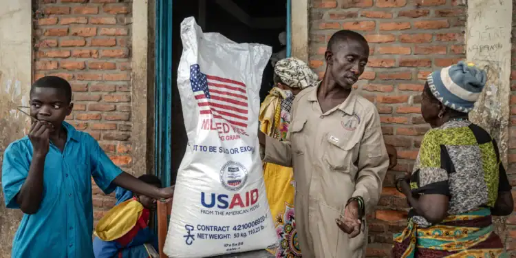 A Burundian government official speaks with newly arrived Congolese refugees awaiting relocation while weighing a sack of rice from the final batches delivered by the now-dismantled US Agency for International Development (USAID). [Luis Tato/AFP]