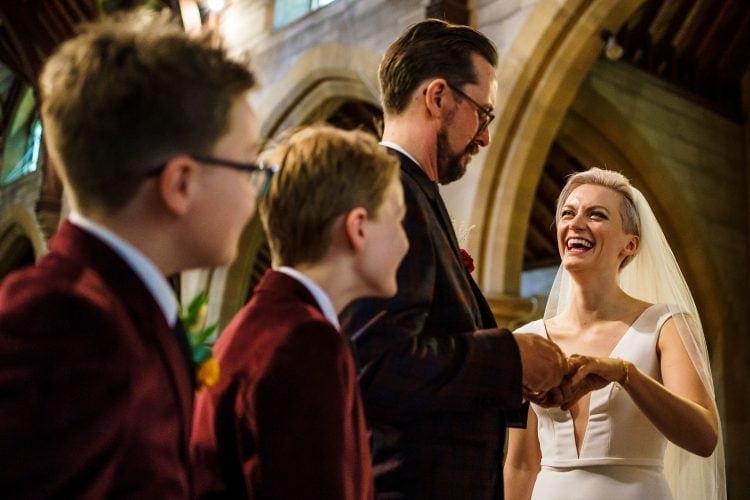 children looking on as the groom has trouble putting the ring on his bride's finger