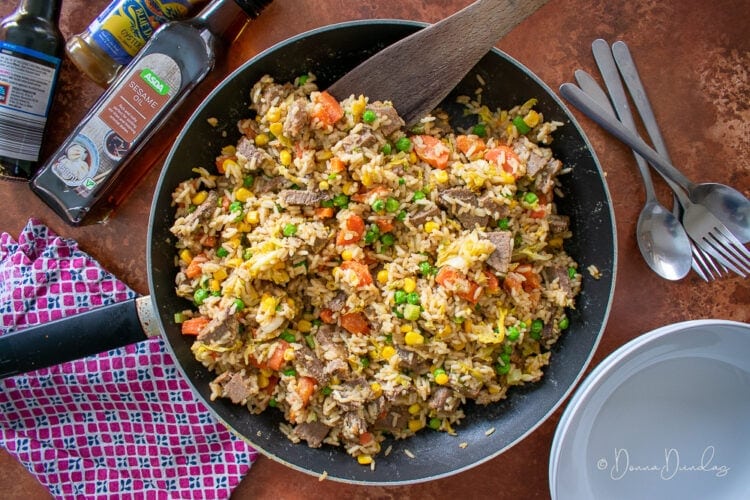 Leftover Roast Beef Fried Rice in frying pan, sesame oil, bowls and spoons to the sides.