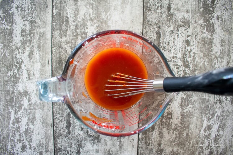 sweet and sour sauce in glass jug with small whisk.