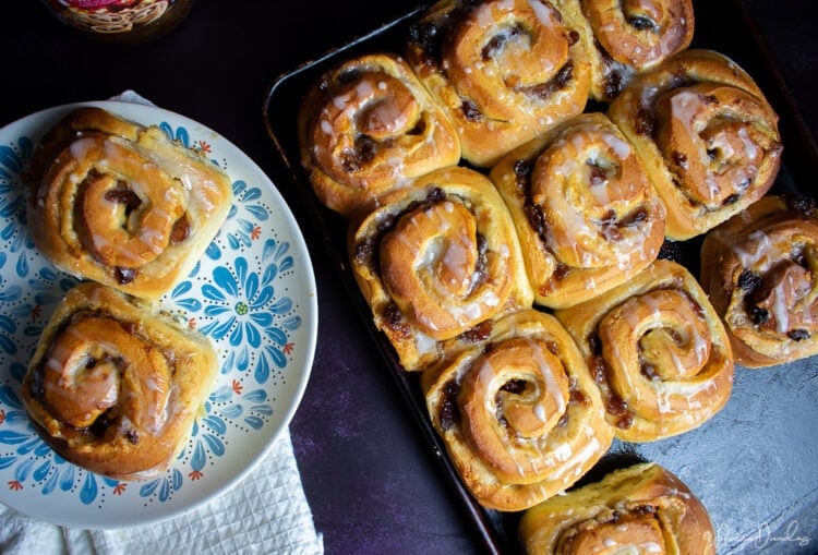 Top view of mincemeat Chelsea buns, some on baking tray, others on patterned plate