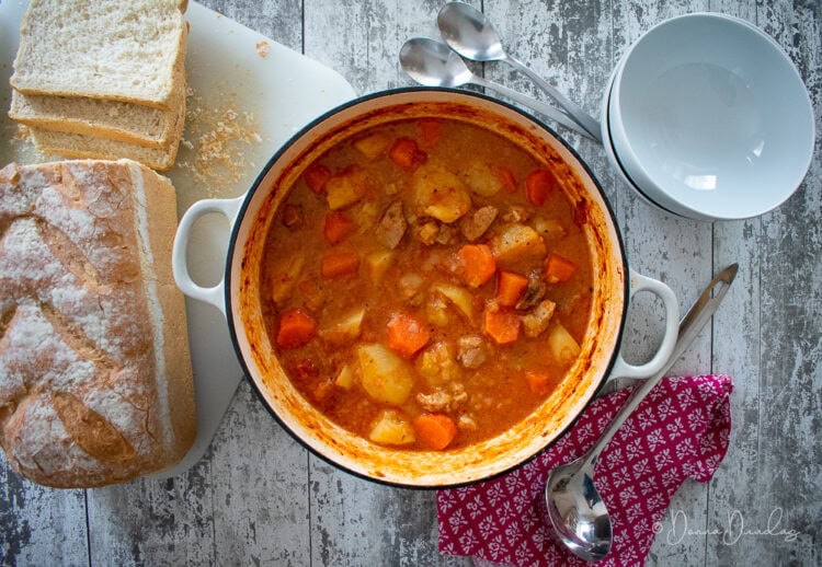 stew in cast iron dish. Loaf on chopping board to the side.