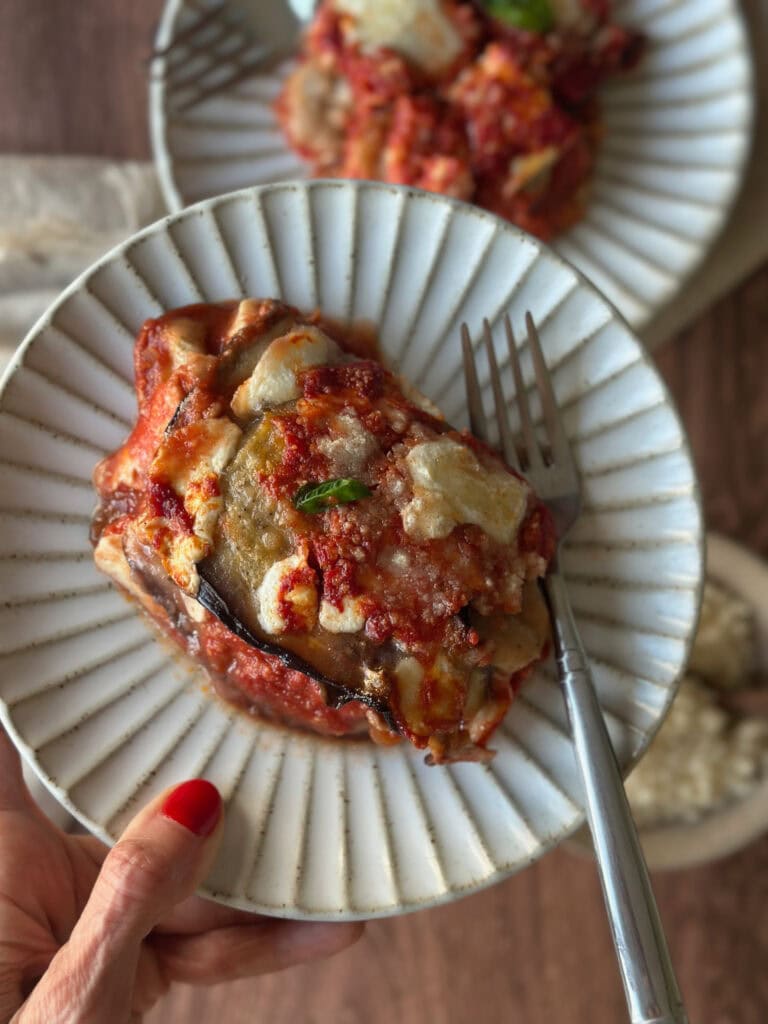 Hand holding a plate of Parmigiana di Melanzane