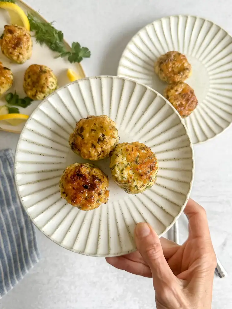 Hand holding scaloppeed plate with 3 meatballs.