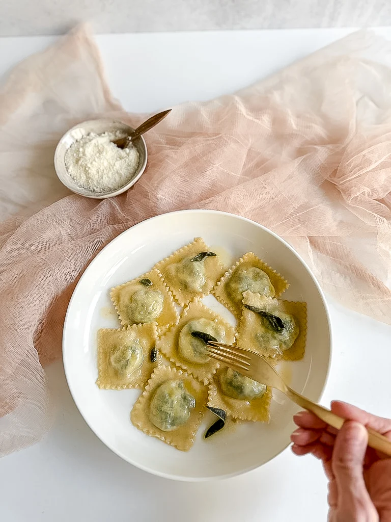 hand holding a fork and breaking up a spinach ricotta ravioli