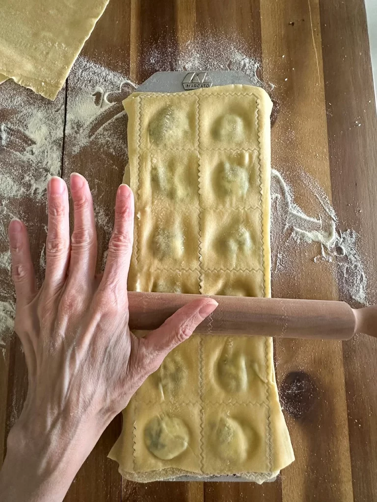 rolling pin on top of closed ravioli in a mold to seal it.