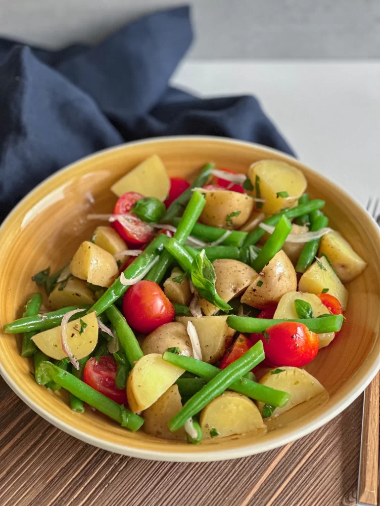 Yellow salad bowl with italian potato salad on a wooden board.