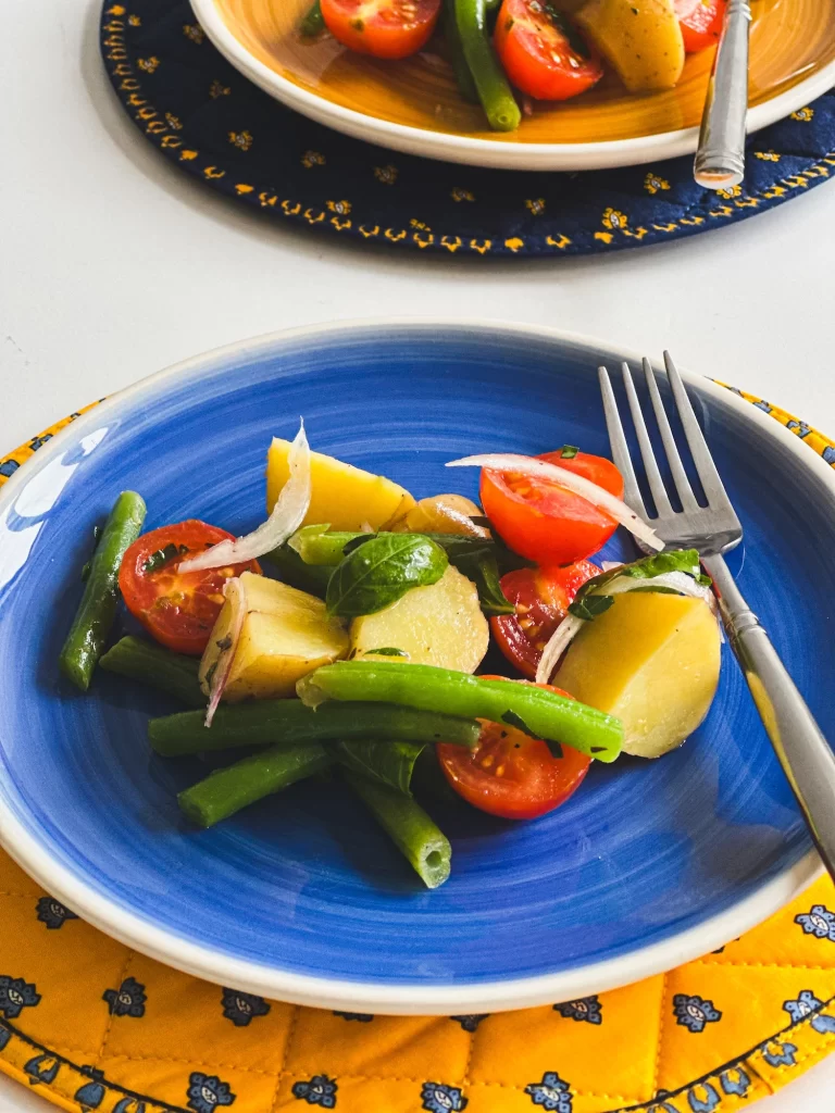 Italian potato green beans salad on a blue plate with a yellow underplate.