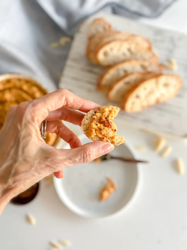 Hand holding a piece of bread with calabrian chili pesto
